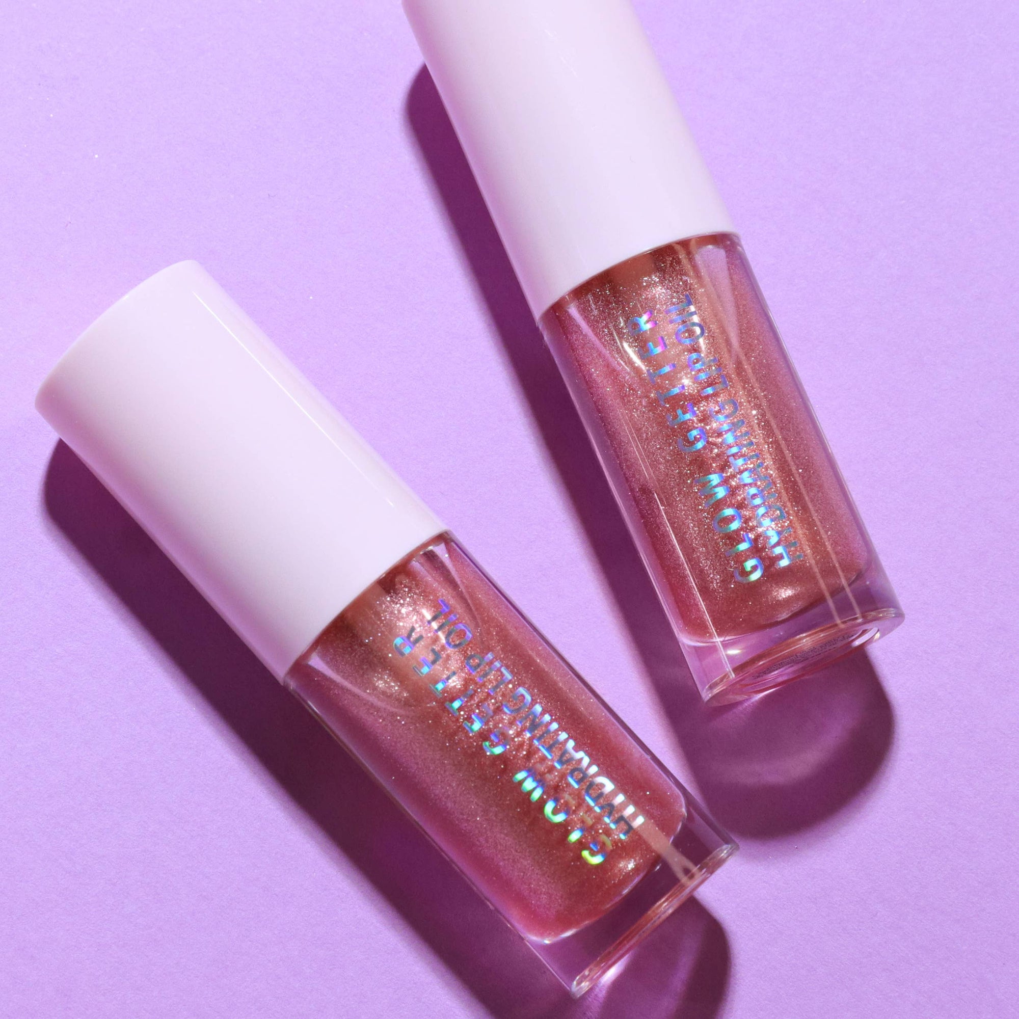 Two lip glosses with glittery finish on a purple background