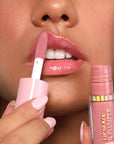 Applying pink lip gloss to their lips with a close-up of the product.